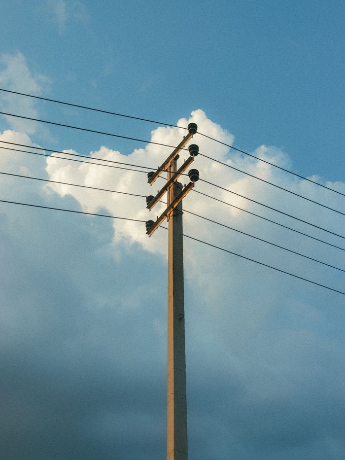 A solitary utility pole with wires against a backdrop of clear blue sky and fluffy clouds.